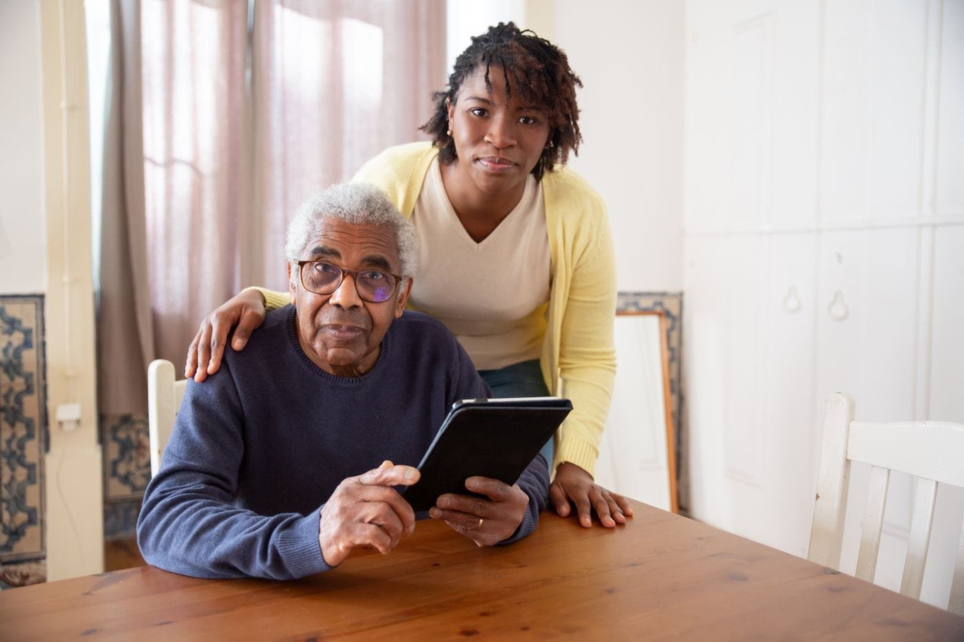 Um homem idoso utiliza um tablet acompanhado por uma mulher